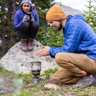 Man warming his hands above the Jetboil MiniMo next to a woman sitting on a rock